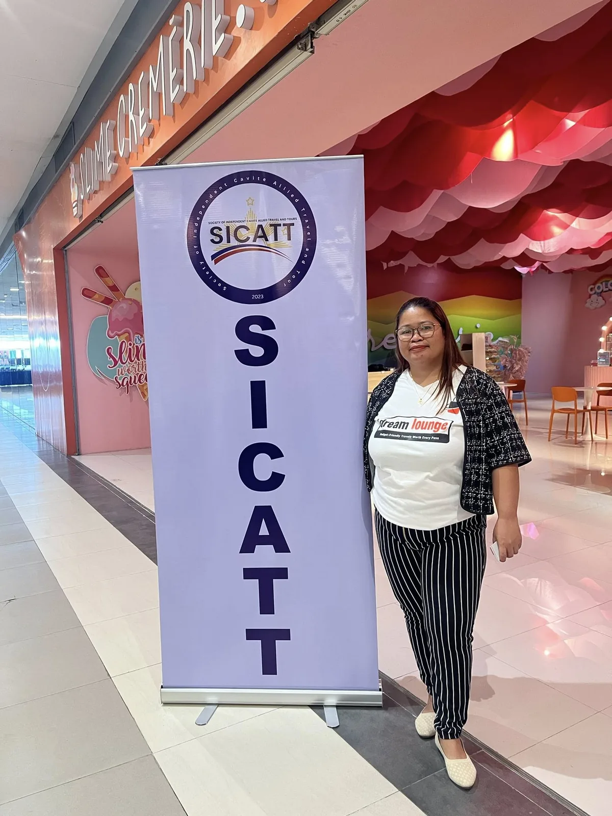 Dream Lounge representative beside a SICATT event banner